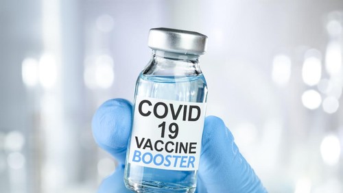 Hand in blue medical gloves holding a vaccine vial with Covid 19 Vaccine Booster text, for Coronavirus booster shot.