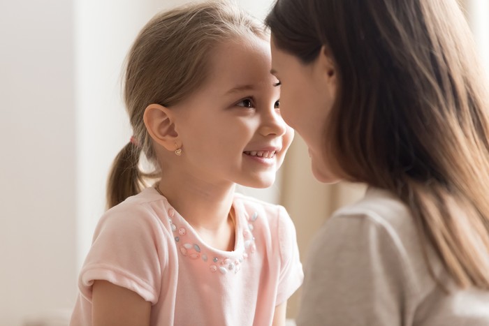 Close up of cute little daughter cuddle with young mom look in eyes enjoy sweet time together, smiling preschooler girl have tender moment with mother or nanny showing love and affection