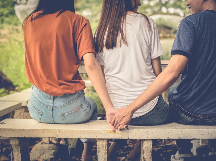 Boyfriend and another woman grab hands from behind together without sight of his girlfriend.. Paramour and divorce concept. Social problem and cheating couples theme. Teen adult and University theme.