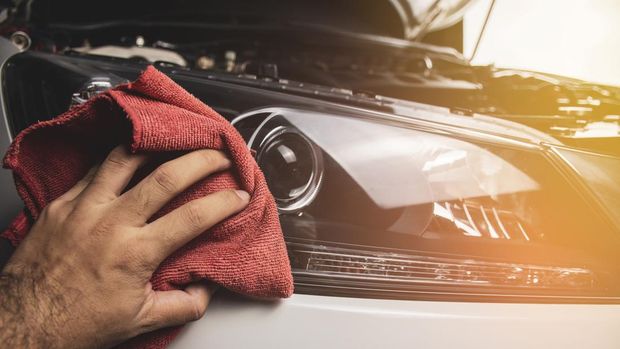 Hand is cleaning car headlight with a using red microfiber cloth,Automotive maintenance concept.