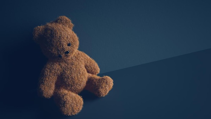 Teddy bear with torn eye sits in dark room. Child abuse and violence concept.