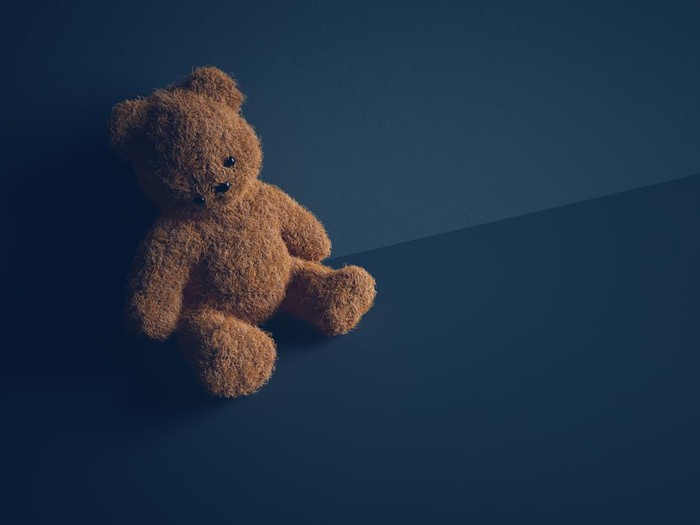 Teddy bear with torn eye sits in dark room. Child abuse and violence concept.