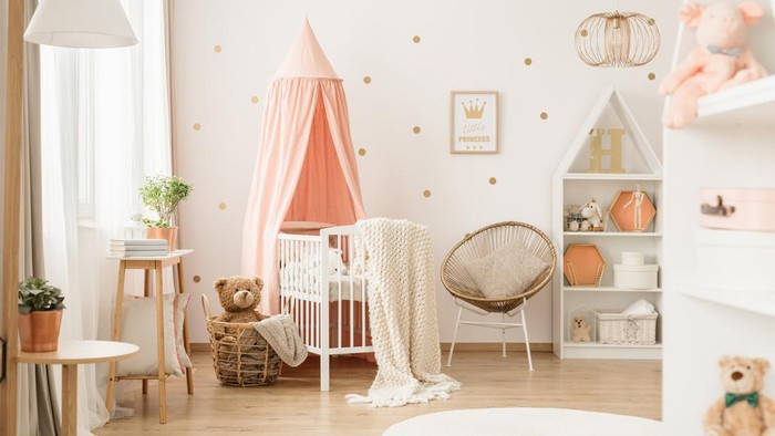 Canopied cradle between gold armchair and basket with teddy bear in pink babys bedroom interior
