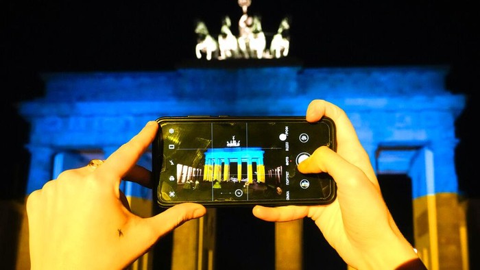 Makin Panas dengan Rusia, Jerman Beri Dukungan ke Ukraina A woman takes a photo of the Brandenburg Gate after it was illuminated in the colours of the Ukrainian flag to show solidarity with the country during the tensions with Russia in Berlin, Germany, Wednesday, Feb. 23, 2022. (AP Photo/Markus Schreiber)