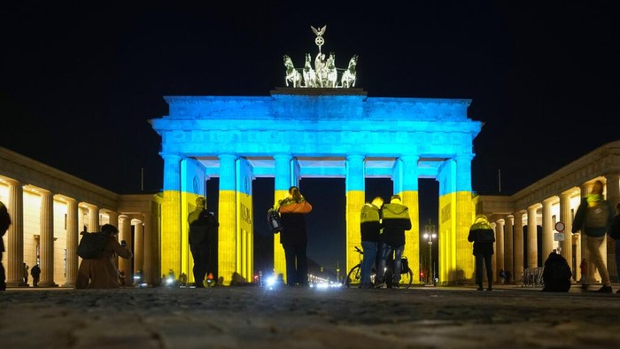A woman takes a photo of the Brandenburg Gate after it was illuminated in the colours of the Ukrainian flag to show solidarity with the country during the tensions with Russia in Berlin, Germany, Wednesday, Feb. 23, 2022. (AP Photo/Markus Schreiber)