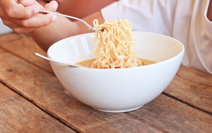 Children eating his instant noodle in white bowl on wood table,Focused on instant noodle.