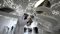 Seorang pria berjubah putih mengambil foto berlatarkan tangga spiral putih dan tulisan kaligrafi museum. (AP/Kamran Jebreili)