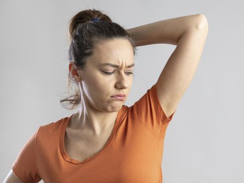 1340848757 Young woman who sniffs armpits and her face is negative on isolated gray background