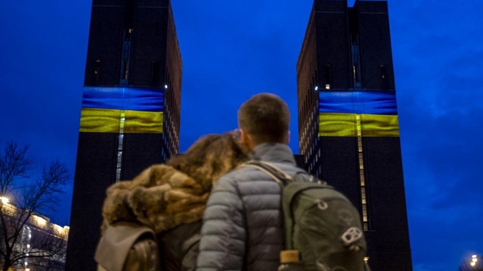 Pasangan di Oslo, AS di depan balai kota menunjukkan video iluminasi bednera Ukraina pada 24 Februari 2022.