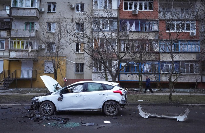 A man walks past a damaged vehicle and debris following Russian shelling in Mariupol, Ukraine, Thursday, Feb. 24, 2022. Russia has launched a barrage of air and missile strikes on Ukraine early Thursday and Ukrainian officials said that Russian troops have rolled into the country from the north, east and south. (AP Photo/Sergei Grits)