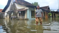 Warga berjalan di depan rumah yang tergenang air di Desa Tanjungkarang, Jati, Kudus, Jawa Tengah, Senin (28/2/2022).