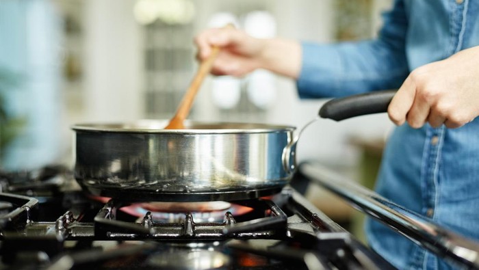 Close-up midsection image of woman cooking food in frying pan. Utensil is placed on gas stove. Female is stirring food in cooking pan. She is preparing food in domestic kitchen.
