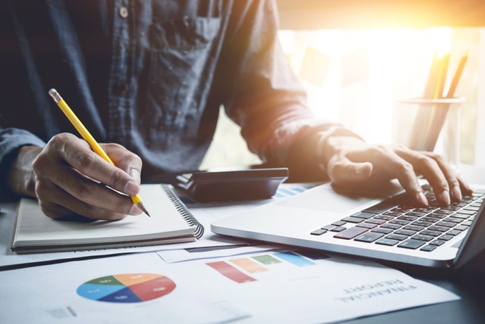 A man analysis business document with laptop computer counting with cost and writing make note at office, Business financial concept
