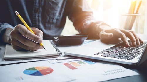 A man analysis business document with laptop computer counting with cost and writing make note at office, Business financial concept