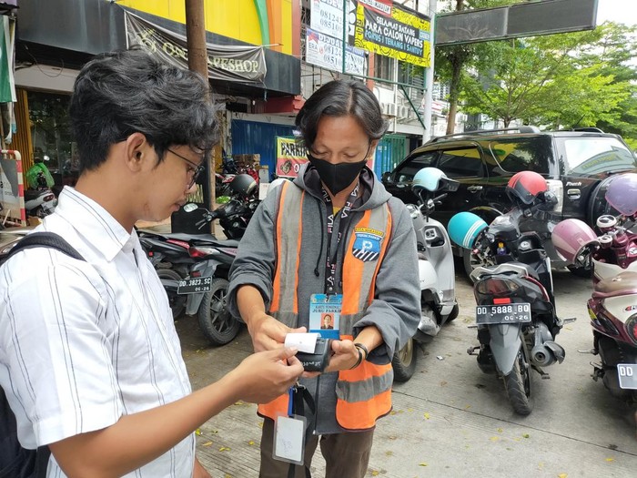 Juru parkir menggunakan alat transaksi berbasis QR Code di Makassar.