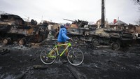 Pesepeda melintas di depan tank Rusia yang hancur. Rentetan ledakan terus terdengar di Kiev, Ukraina, menyusul gempuran militer Rusia ke ibu kota pada Rabu (2/3) malam. (AP Photo/Serhii Nuzhnenko)