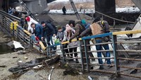 Mereka melintasi jembatan yang hancur setelah diledakkan oleh militer Ukraina.