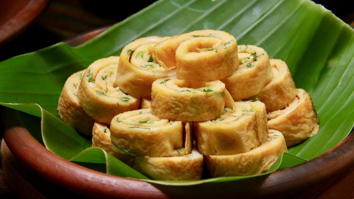 Telur Dadar, the egg omelet with scallion slices. the omelet is rolled then sliced into spirals. The spirals are stacked and mounted on an earthenware plate lined with banana leaf.
