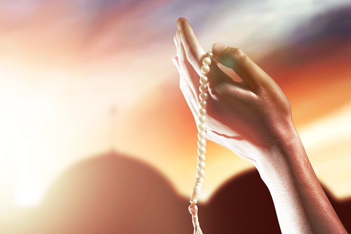 Muslim man praying with prayer beads on his hands with dramatic sky background