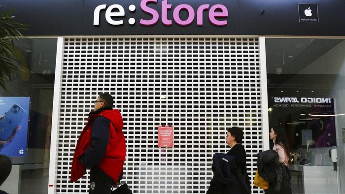 Visitors walk past a closed 're:Store', an Apple reseller shop in a shopping mall in Omsk, Russia, Wednesday, March 2, 2022. Apple on Tuesday announced halting the sales of its iPhone and other popular products in Russia as part of an intensifying corporate crackdown spurred by the country's invasion of Ukraine. Stores of the re:Store chain, the company's official reseller in Russia, didn't open on Wednesday, citing the need to reassess the situation. (AP Photo/Evgeniy Sofiychuk)
