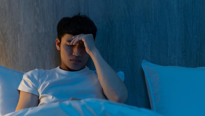 close up of asian young man is worrying about something on bed at night