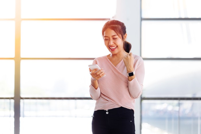 Young Asian girl looking at her mobile phone and get excited inside the building. One beautiful woman is happy watching at smartphone indoors.