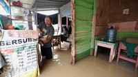 Pemilik warung makan melayani pembeli di depan rumahnya yang tergenang banjir di Kota Baru, Jambi, Minggu (6/3/2022).