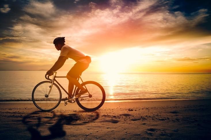 Ilustrasi bersepeda di pantai saat senja.