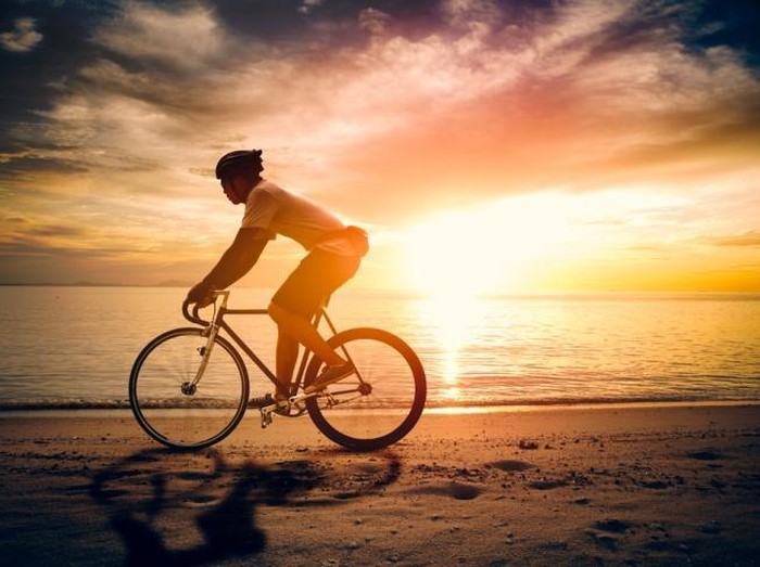 Ilustrasi bersepeda di pantai saat senja.