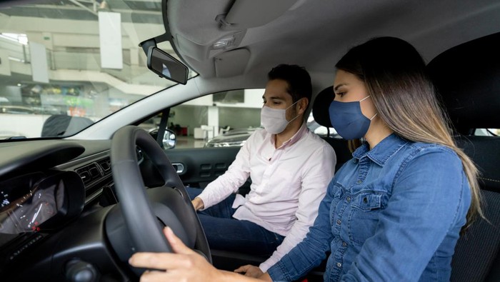Latin American woman talking to a salesman and wearing facemasks while buying a car at the dealership during the COVID-19 pandemic