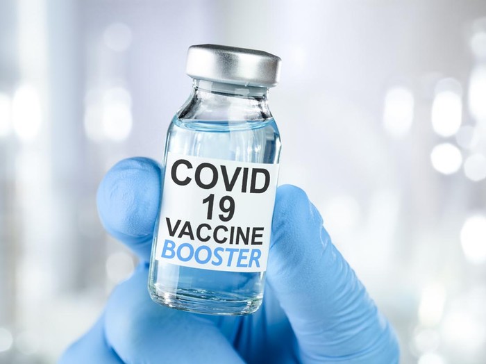 Hand in blue medical gloves holding a vaccine vial with Covid 19 Vaccine Booster text, for Coronavirus booster shot.