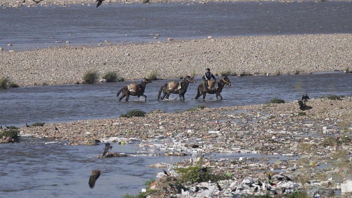 A man collects sand on horse backs and moves past the polluted banks of River Tawi in Jammu, India, Wednesday, March 9, 2022.(AP Photo/Channi Anand)