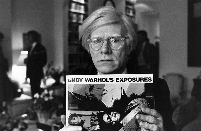 Andy Warhol (1926 - 1987), American pop artist and filmmaker, holding an example of one of his posters.  Original Publication: People Disc - HM0195   (Photo by John Minihan/Getty Images)