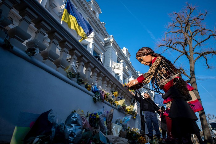 LONDON, ENGLAND - MARCH 10: The Little Amal puppet lays flowers outside the Ukrainian Embassy on March 10, 2022 in London, England. Little Amal is a 3.5 metre tall puppet representing refugee children. Last year she walked 8000 miles around Europe to raise awareness of their plight.  (Photo by Chris J Ratcliffe/Getty Images)
