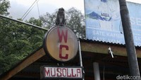 Seekor monyet ekor panjang berada di atas plang bertuliskan WC di kawasan Puncak, Cisarua.