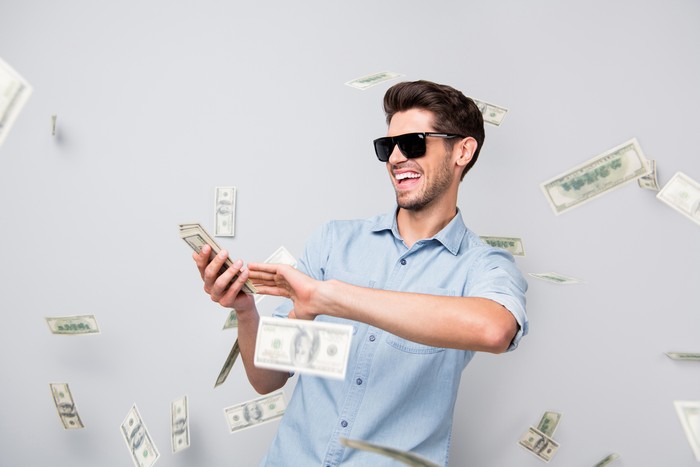 Ilustasi kaya Photo of cheerful excited ecstatic overjoyed man throwing money away, showing his wealthiness wearing denim isolated over grey color background