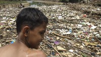Seorang bocah melihat sampah yang terbawa aliran air dan menyangkut di salah satu jembatan di Kali Pesanggrahan, Cipayung, Depok, Jawa Barat, Jumat (11/3/2022).