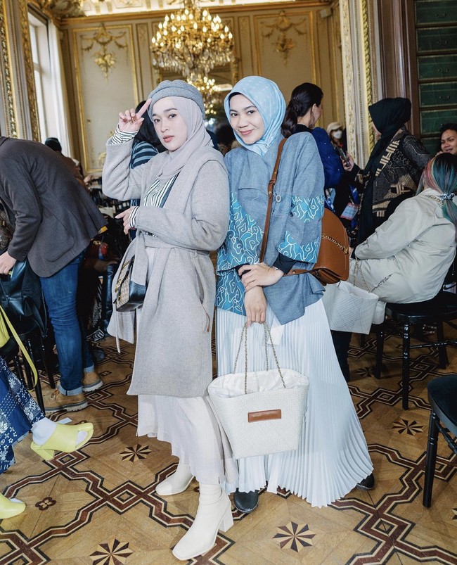Saat menghadiri fashion show di Paris, Ririe Fairus terlihat edgy dengan long coat abu-abu, sling bag, rok putih, dipadu dengan ankle boots putih. Sementara Mommy ASF, Eka Nur Prasetyawati tampil feminin dengan blouse batik biru dan rok pleats putih. Foto: Dok. Instagram @ririe_fairuz.