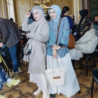 Saat menghadiri fashion show di Paris, Ririe Fairus terlihat edgy dengan long coat abu-abu, sling bag, rok putih, dipadu dengan ankle boots putih. Sementara Mommy ASF, Eka Nur Prasetyawati tampil feminin dengan blouse batik biru dan rok pleats putih. Foto: Dok. Instagram @ririe_fairuz.