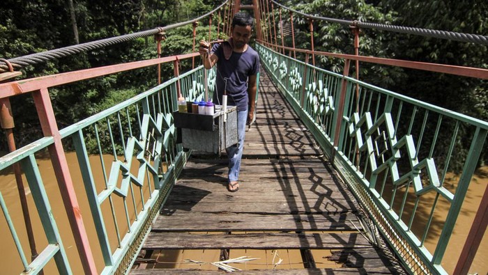 Warga berjalan melintasi jembatan yang berlubang di Jembatan Wiratman, Srengseng Sawah, Jakarta, Sabtu (12/3/2022). Jembatan yang menghubungkan Kelurahan Srengseng Sawah, Jakarta Selatan dengan Kelurahan Pasir Gunung Selatan, Depok tersebut mengalami kerusakan pada papan pijak yang mulai berlubang serta besi yang berkarat sehingga dapat membahayakan warga yang melintas. ANTARA FOTO/Asprilla Dwi Adha/rwa.