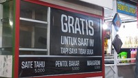 Spanduk tulisan ‘gratis untuk hari ini’, gerobak jajanan yang menjual sate tahu,  pentol bakar dan makaroni ini punya tulisan lanjutan di bawahnya yang bikin orang emosi sekaligus ngakak. Foto: Twitter/Site