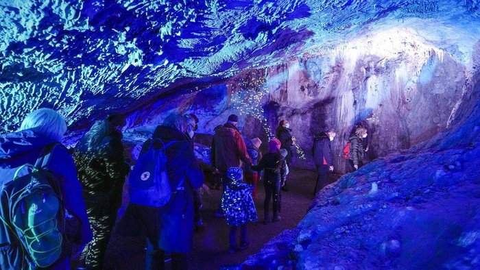 People visit the colorful, illuminated Dechen Cave in Iserlohn, Germany, Friday, March 11, 2022. The cave, which was discovered by two railway workers in 1868, is temporarily illuminated by light artist Wolfgang Flammersfeld. (AP Photo/Martin Meissner)