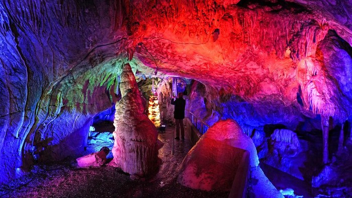People visit the colorful, illuminated Dechen Cave in Iserlohn, Germany, Friday, March 11, 2022. The cave, which was discovered by two railway workers in 1868, is temporarily illuminated by light artist Wolfgang Flammersfeld. (AP Photo/Martin Meissner)