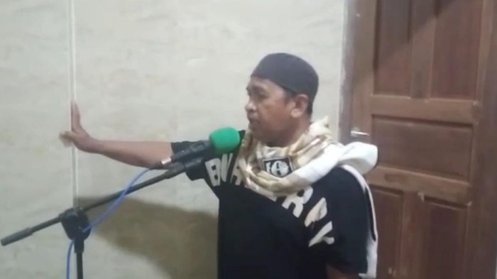 Seorang warga mengumumkan penolakan kebijakan penggantian ketua RT/RW di masjid.