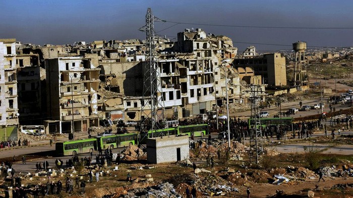 FILE - In this photo released by the Syrian official news agency SANA, residents gather near green government buses for evacuation from eastern Aleppo, Syria, Thursday, Dec. 15, 2016. Tuesday, March 15, 2022 marks the 11th anniversary of Syria's revolution-turned-civil war. This year, many survivors are watching in shock as Ukrainians face the same horrors they did. (SANA via AP, File)