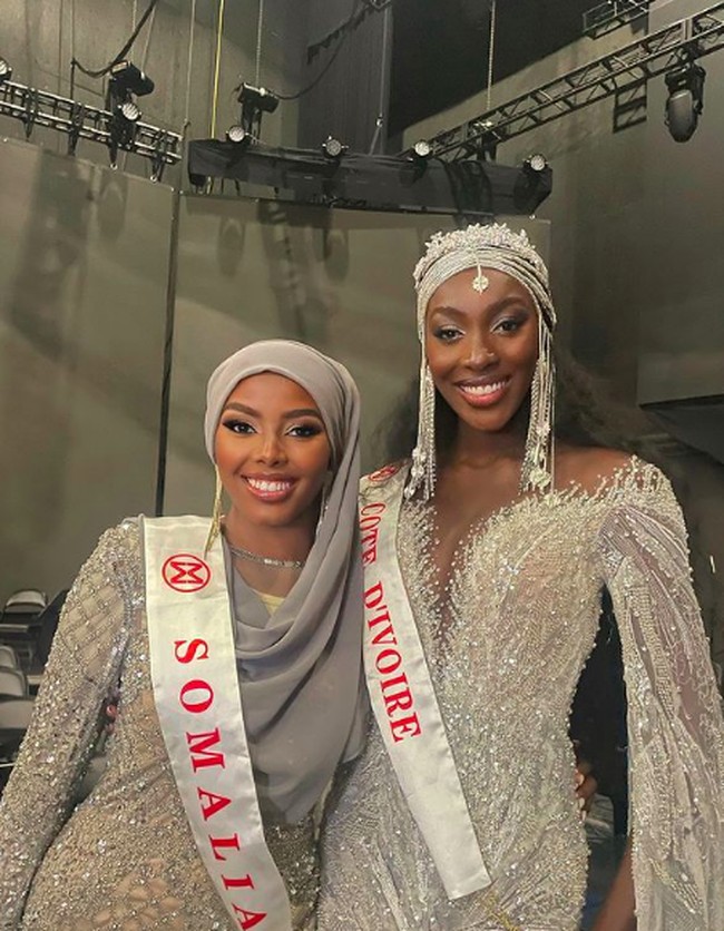 Inilah penampilan Khadija Omar di Miss World 2021. Gaun silvernya ini digunakan di kontes gaun malam Miss World 2021. Dalam potretnya, Khadija berpose bersama Olivia Yace yang merupakan Miss Cote D’Ivoire 2021. Foto: Instagram