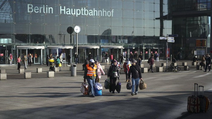 Potret Stasiun Kereta Berlin yang Dipenuhi Pengungsi Ukraina A volunteer in a red vest helps refugees from the Ukraine after they arrived at the main train station in Berlin, Germany, Wednesday, March 16, 2022. The Ukraine war has turned the basement of Berlinβs glass-and-steel main train station into a sprawling refugee town where a small army of volunteers in yellow and orange vests offer everything from shampoo to cell phone chargers to exhausted refugees. Sign in the background reads: Berlin Main Station. (AP Photo/Markus Schreiber)