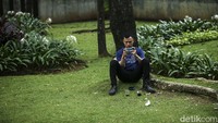 Seorang warga beristirahat sambil duduk santai di bawah pohon Taman Suryo, Jakarta.