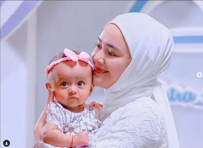 Acara akikah anak Amanda Manopo di Ikatan Cinta dibuat dengan dekorasi bernuansa putih dan biru. Amanda mengenakan busana muslim dipadu dengan hijab pashmina warna putih yang diikat rapi ke belakang. Foto: Dok. Instagram @i_yoora05.