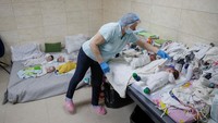 Di ruang bawah tanah yang sepi, para perawat sibuk menggendong, menidurkan, dan mengajak bermain puluhan bayi.